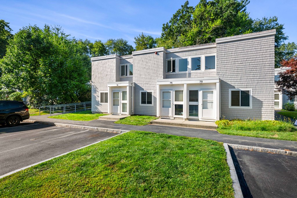 the exterior of a white house with a parking lot and grass