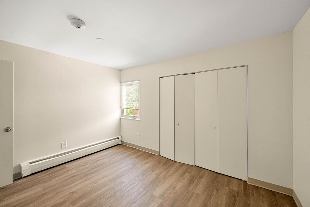 a bedroom with white walls and wood floors and a window