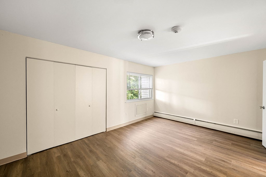 a bedroom with white walls and wood floors and a window
