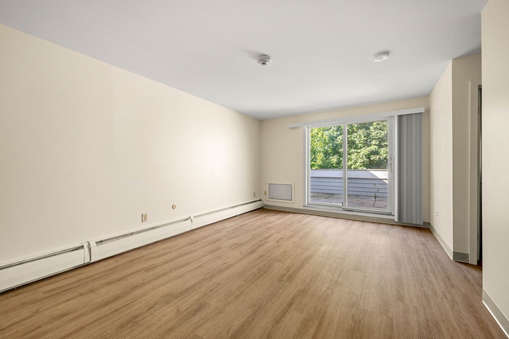 the living room of an empty house with wood flooring and a large window
