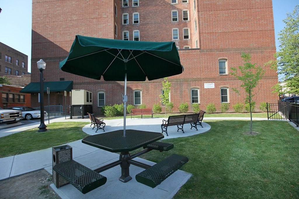 a picnic table with an umbrella and benches in a courtyard