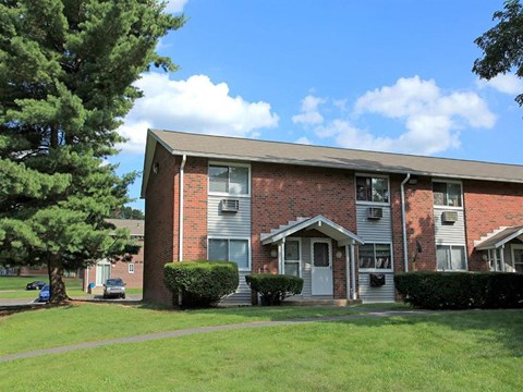 a brick apartment building with a green lawn and trees