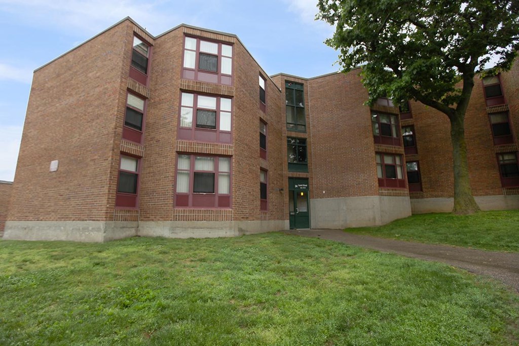 a large brick building with a green lawn and a tree