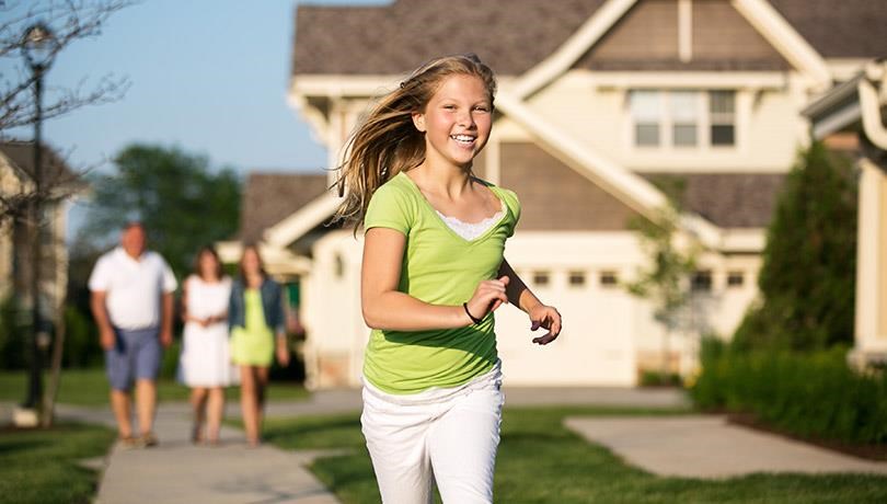 a young girl running down a sidewalk in front of a house
