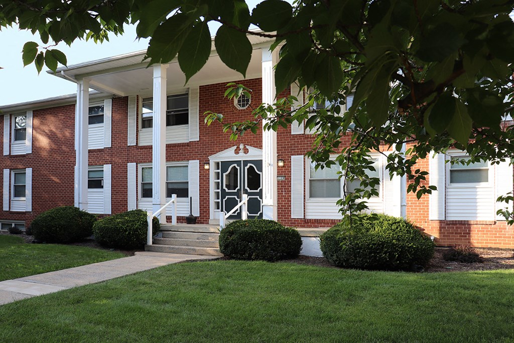 the front of a brick building with white pillars and a lawn