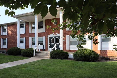 the front of a brick building with white pillars and a lawn