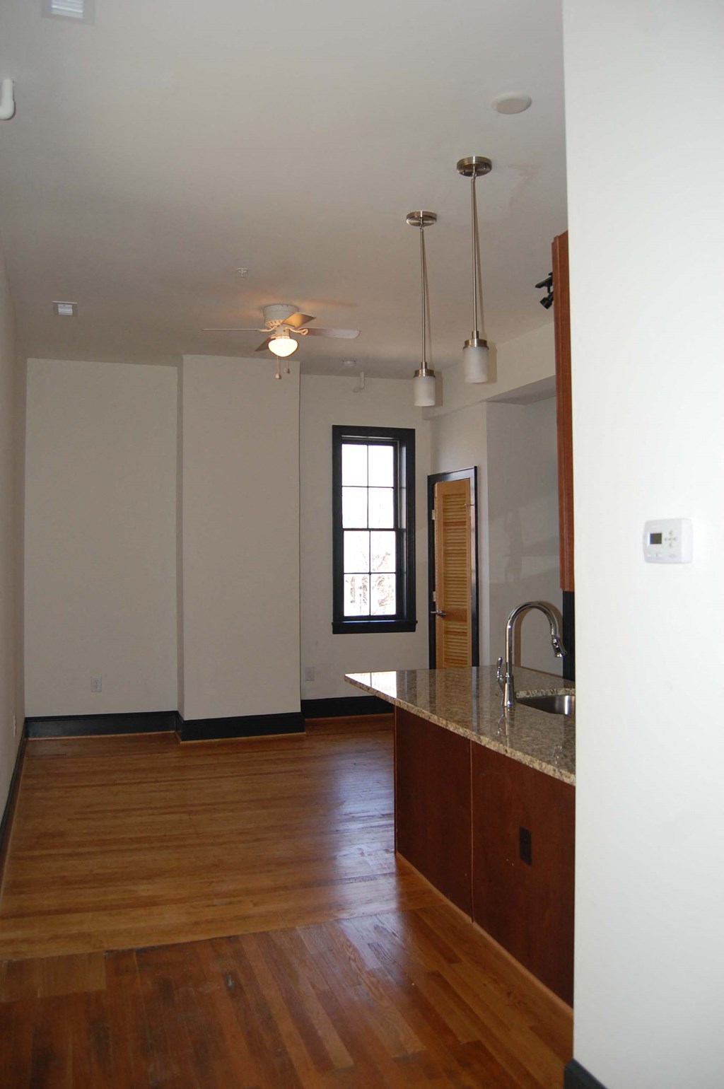 an empty living room and kitchen with wood floors and white walls