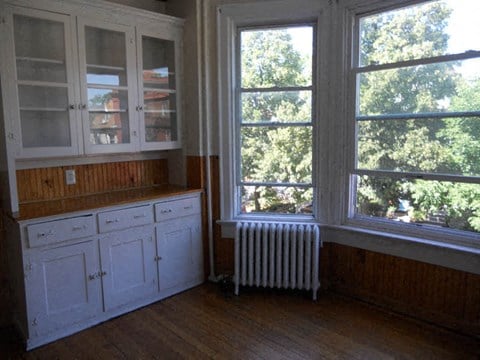 a kitchen with white cabinets and a radiator and large windows