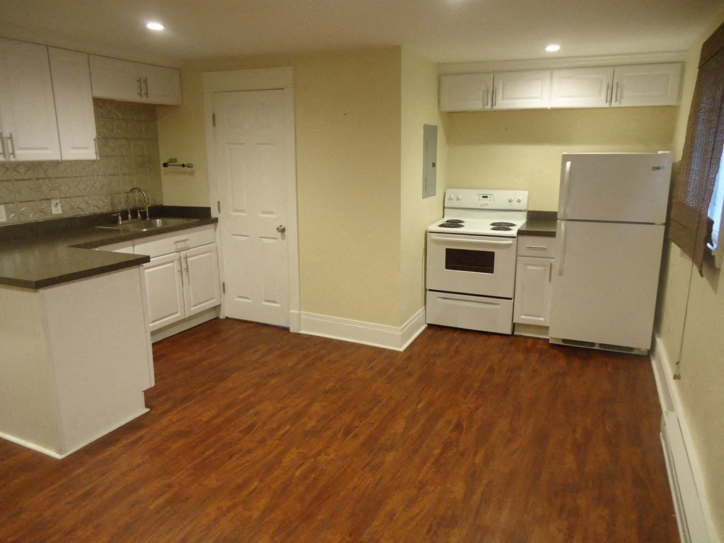 an empty kitchen with white appliances and a wooden floor