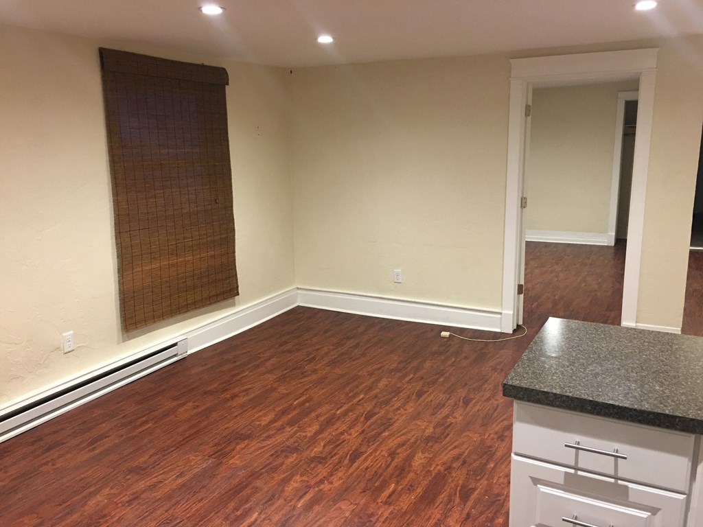 an empty living room with wood flooring and a kitchen