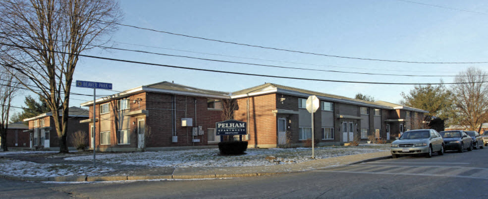 A car is parked in front of a brick building with a sign that reads "Pelham".