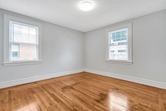 an empty bedroom with wood floors and two windows
