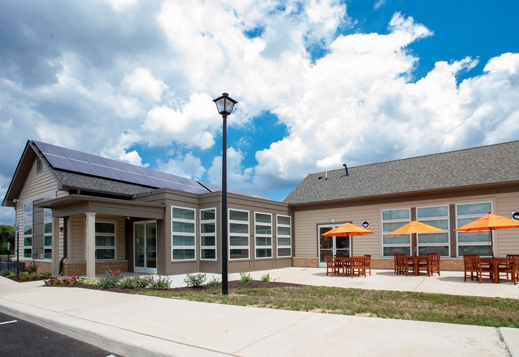 the front of a building with tables and umbrellas and solar panels