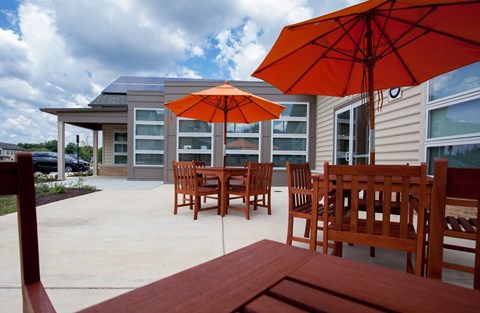 a patio with tables and umbrellas in front of a house