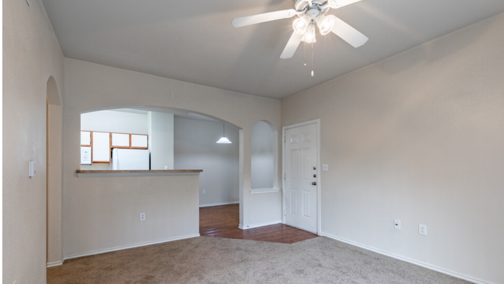 an empty living room with a ceiling fan and a kitchen