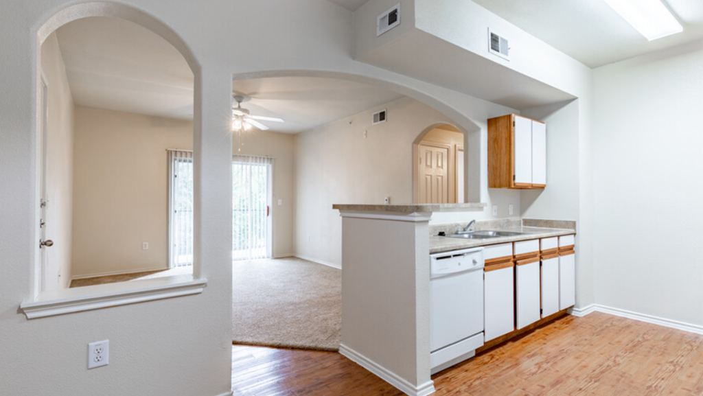 an empty living room and kitchen with an archway into the living room