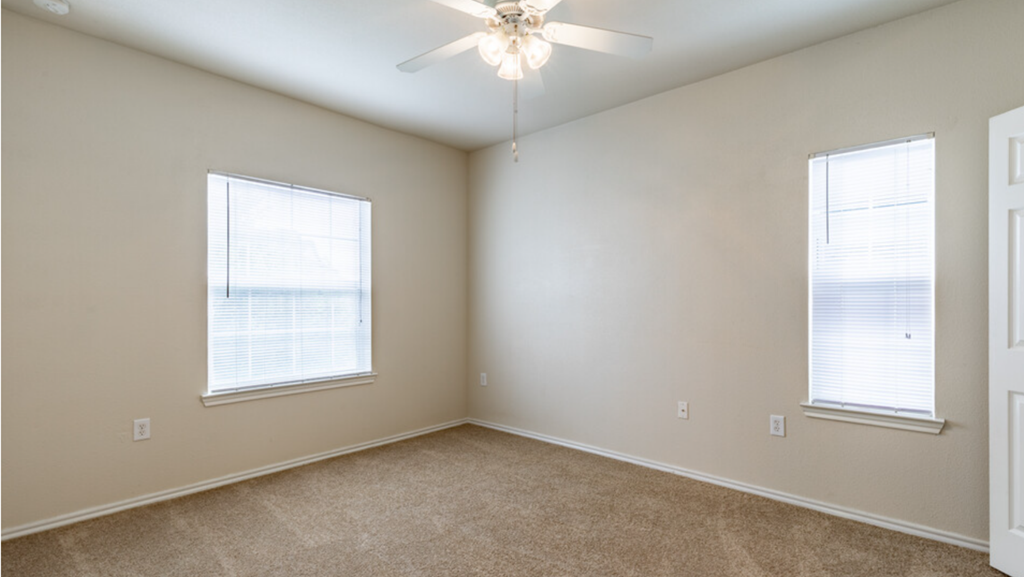 an empty bedroom with two windows and a ceiling fan