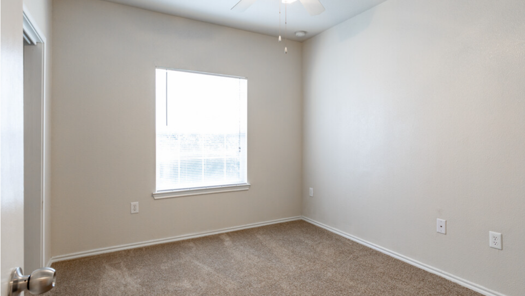 an empty bedroom with a window and carpeting