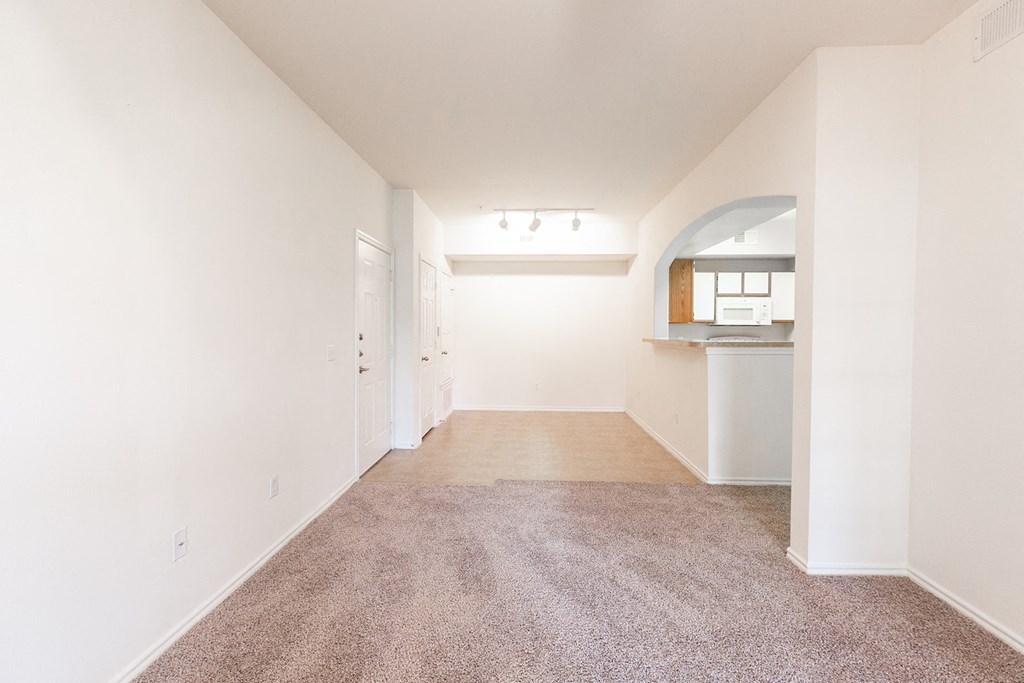 an empty living room with white walls and carpet and a kitchen