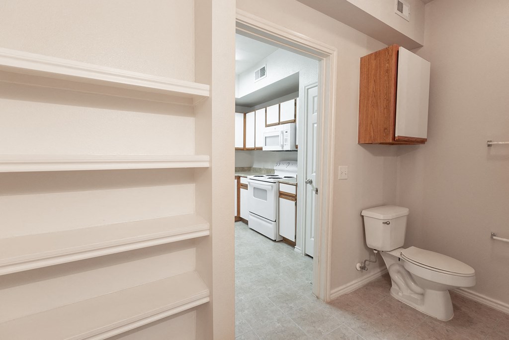 a bathroom with white cabinets and a toilet and a kitchen