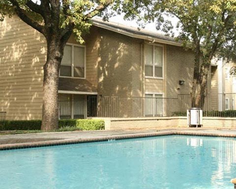 A pool in front of a tan building with a tree in front of it.