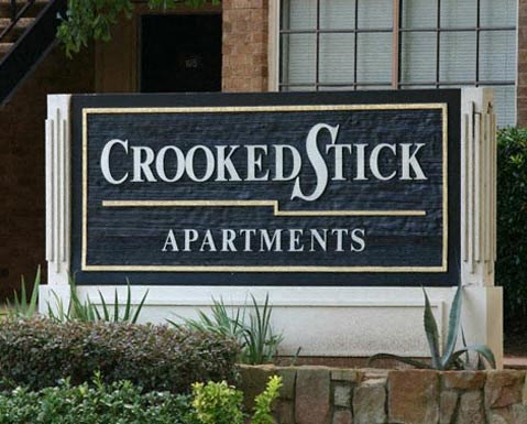 A sign for Crooked Stick Apartments is displayed in front of a building.