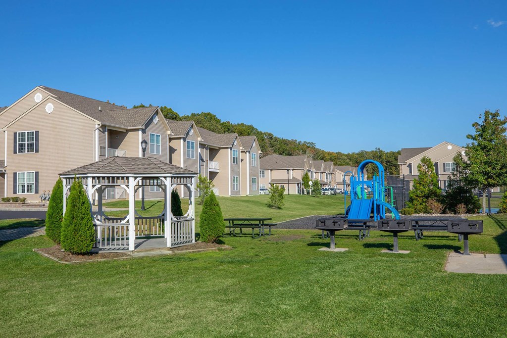 a gazebo and picnic tables in a park with apartments in the background