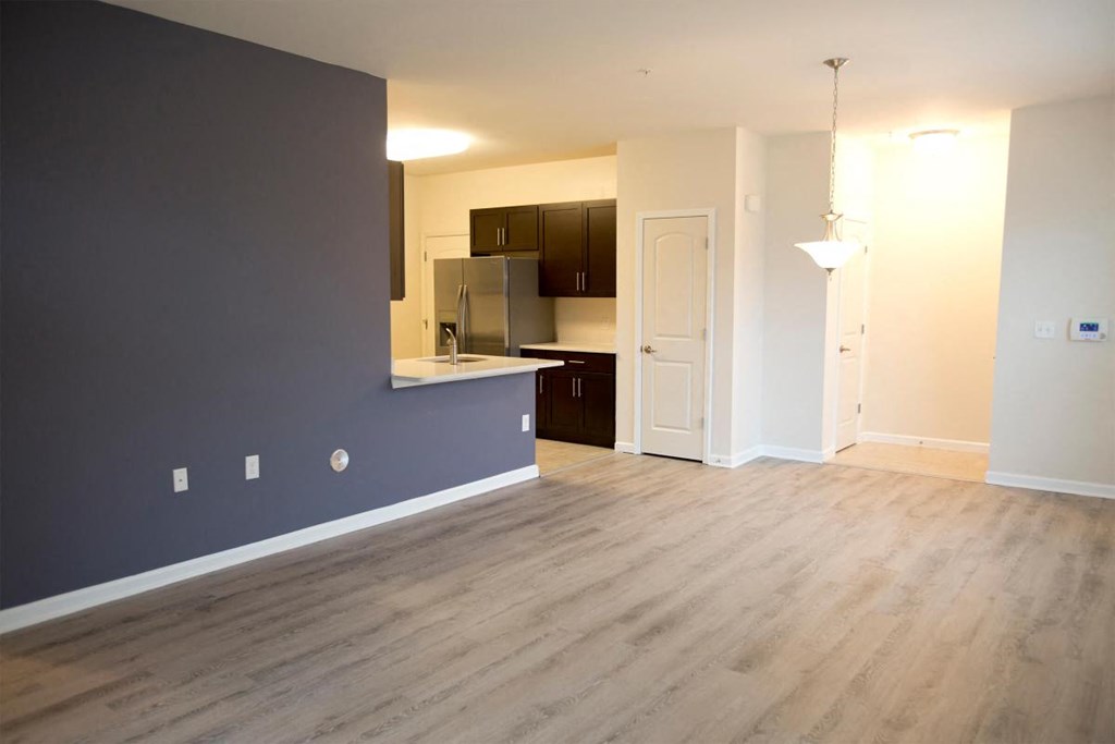 an empty living room with a blue accent wall and a kitchen