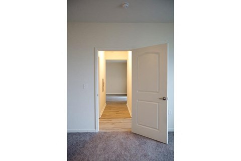 the door is open to a hallway with a door to a bedroom