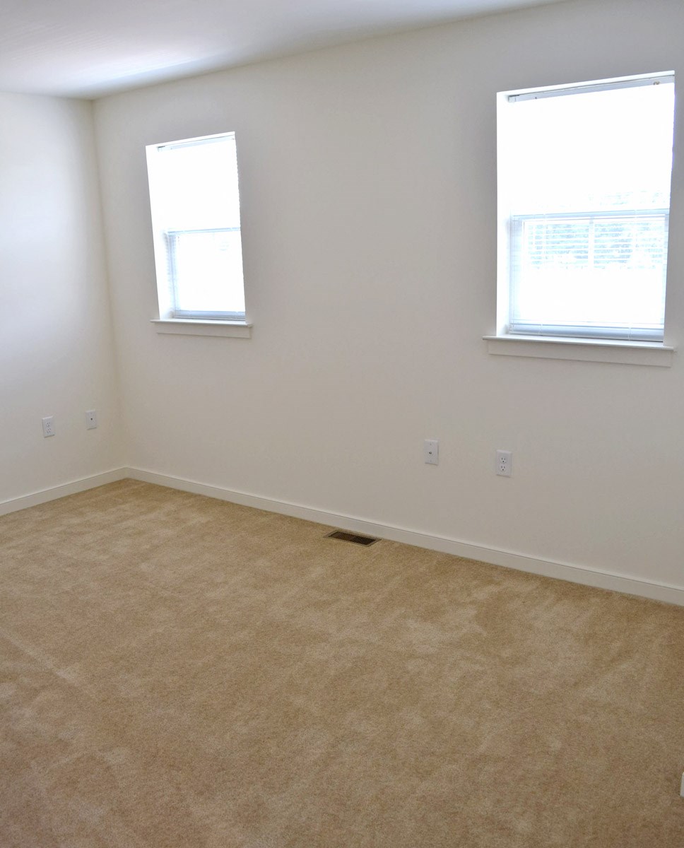 an empty room with two windows and a carpeted floor