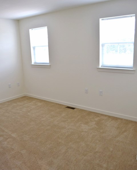 an empty room with two windows and a carpeted floor