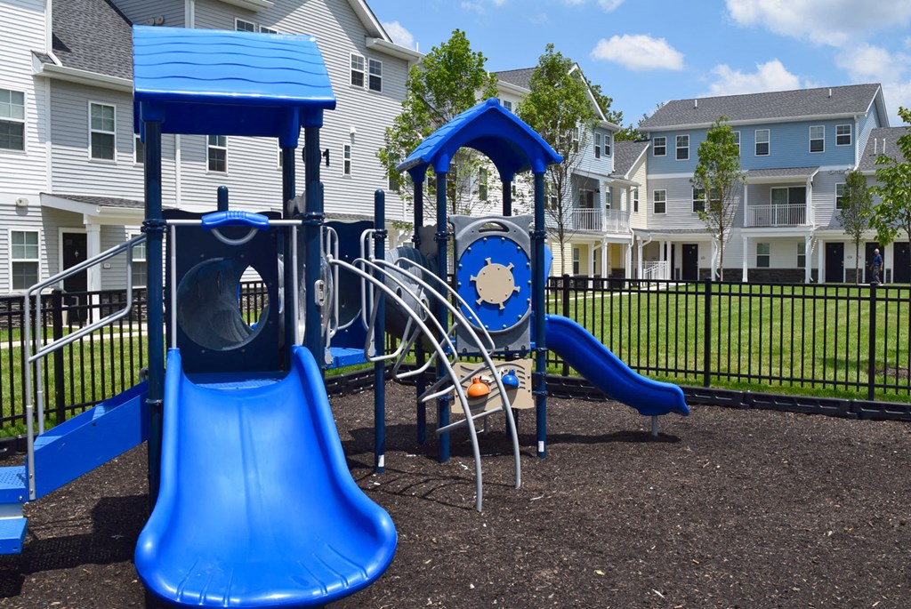 a playground with a blue playset and slides in front of houses