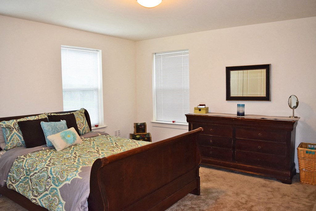 a bedroom with a bed and dresser and two windows
