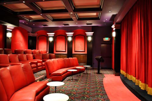 a theater room with red chairs and a red curtain