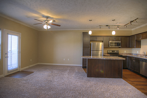 an empty living room with a kitchen and a ceiling fan