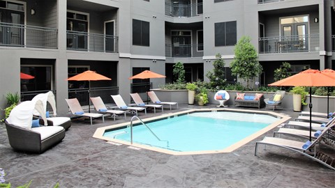 a swimming pool in a courtyard with chairs and umbrellas