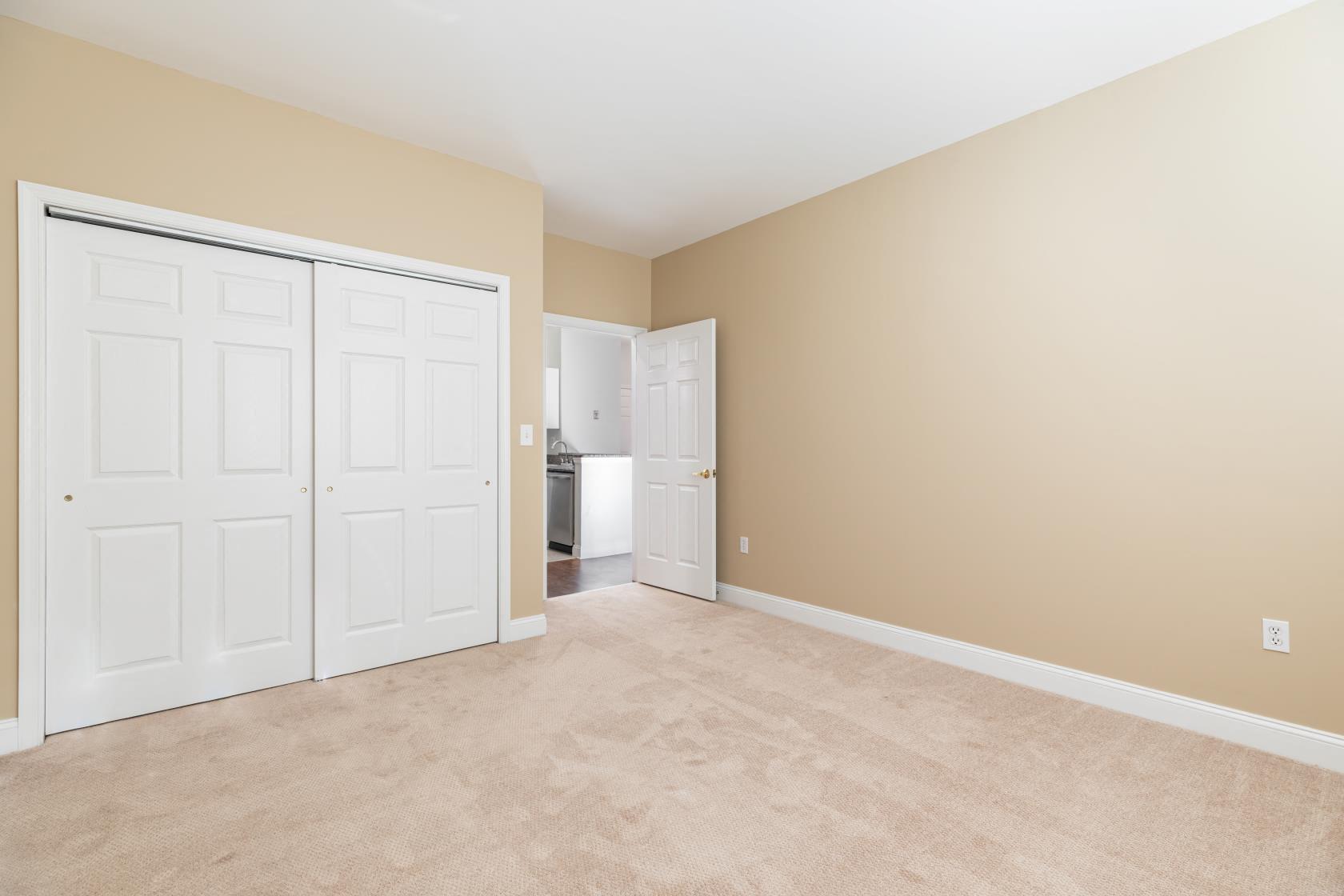 an empty living room with a closet and a door to a kitchen