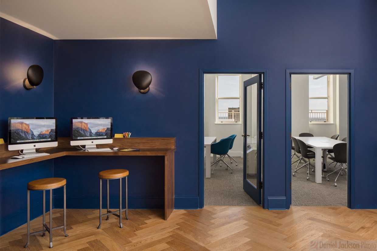 a room with a desk with two computers and a table with chairs
