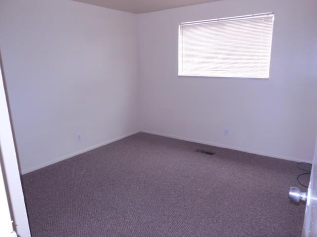 an empty room with a window and gray carpet