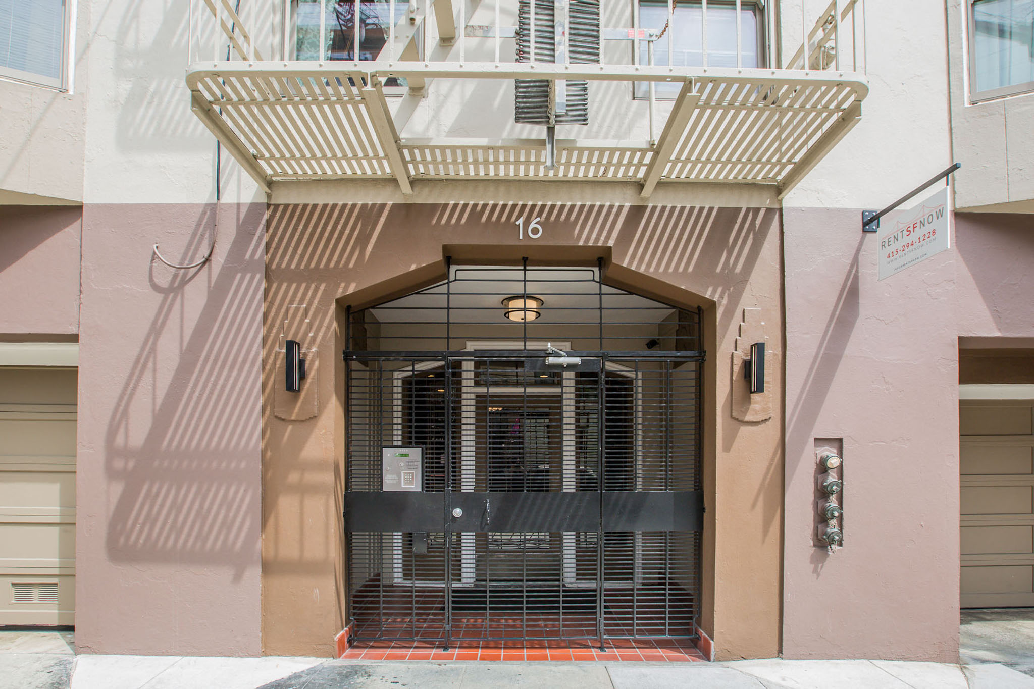 A building with a pink facade has a large gate in front of it.
