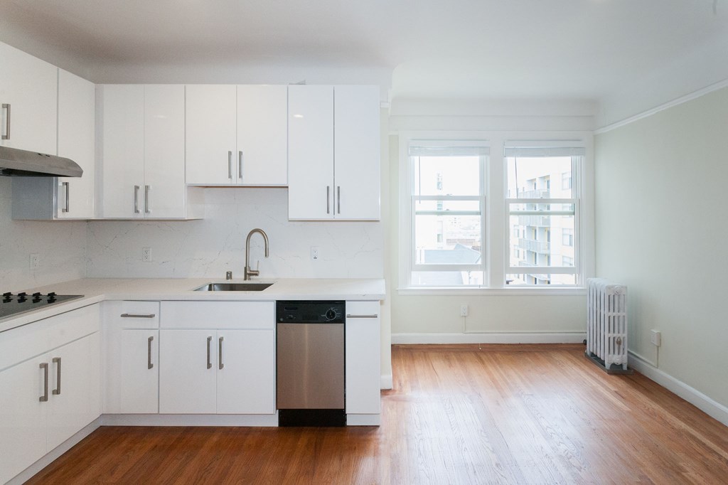 A kitchen with white cabinets and a wooden floor.