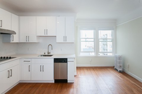 an empty kitchen with white cabinets and a window