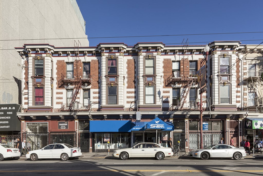 A row of old buildings with cars parked in front.