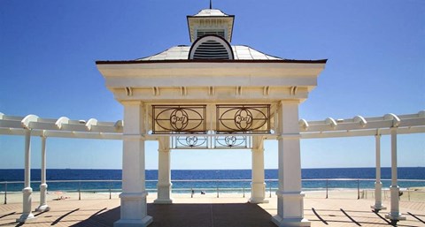 A gazebo with a clock on the front is situated on a beach.
