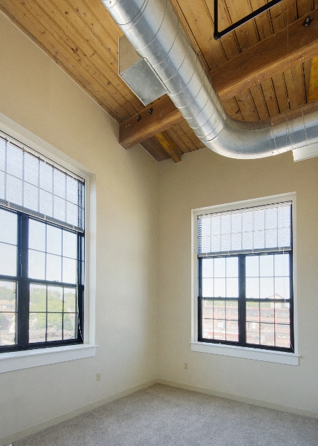 an empty room with two windows and a pipe on the ceiling