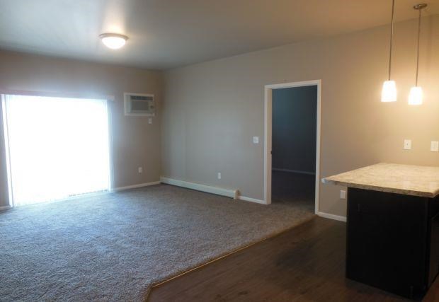 an empty living room with a door to a kitchen