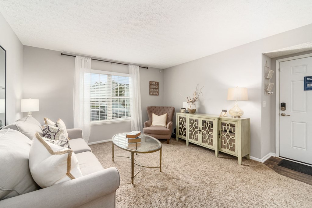 A living room with a white couch, a coffee table, and a window with curtains.