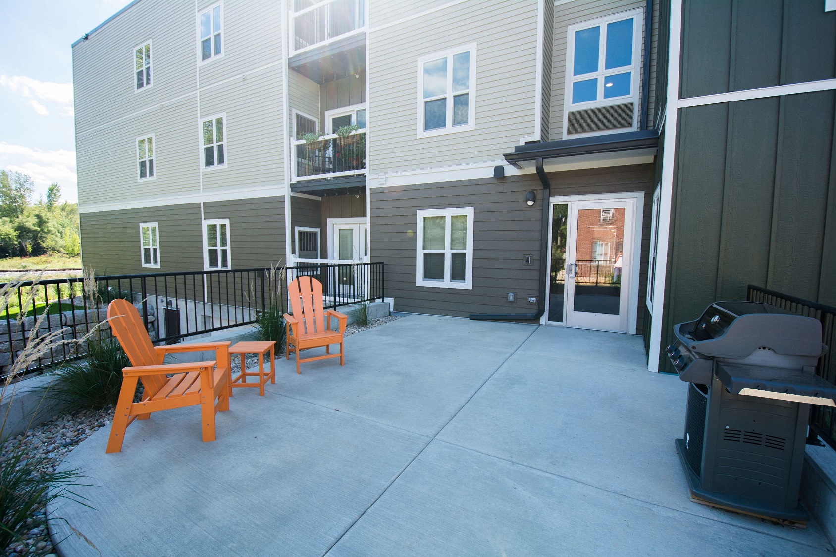 a patio with orange chairs and a grill in front of an apartment building