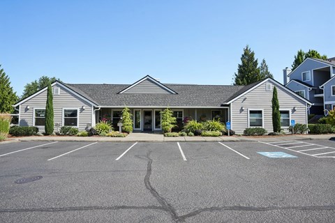 A parking lot in front of a grey building with a clear blue sky.
