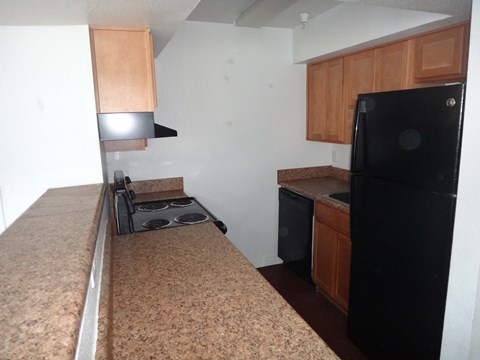 A kitchen with a black refrigerator, brown countertop, and wooden cabinets.